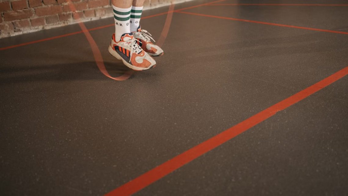 Feet of a person in sneakers skipping rope on an indoor gym floor.