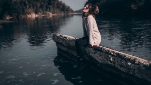 A woman enjoys a peaceful moment sitting on a riverside barrier during sunset.