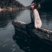 A woman enjoys a peaceful moment sitting on a riverside barrier during sunset.